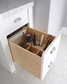 an open drawer in a kitchen with hair dryers and other items inside it on the counter