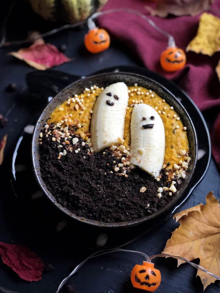 two bananas with faces carved into them sitting in a bowl surrounded by pumpkins and leaves