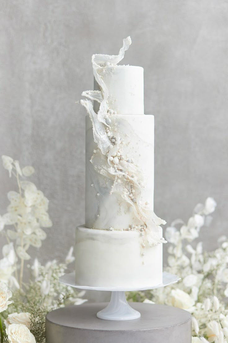 a three tiered white wedding cake with flowers in the background