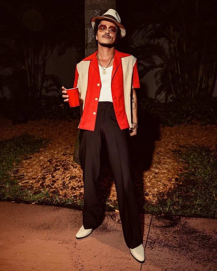 a man in a red jacket and white shirt standing next to a tree at night