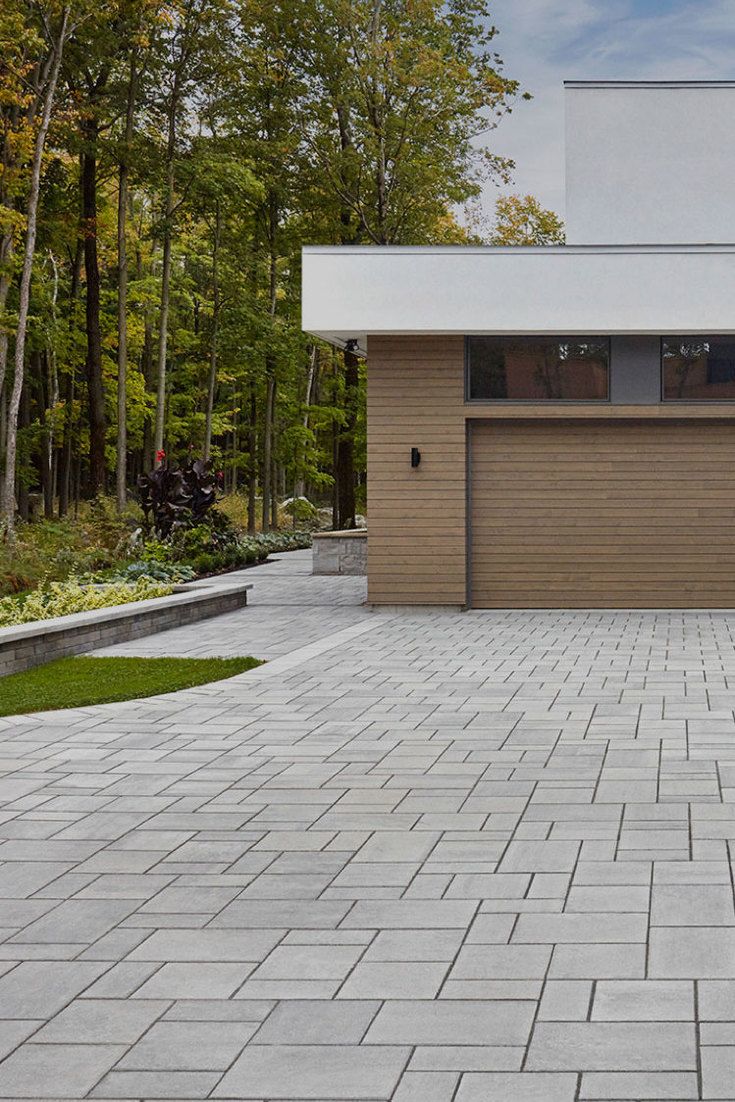 a large brick driveway with a garage door on one side and trees in the background