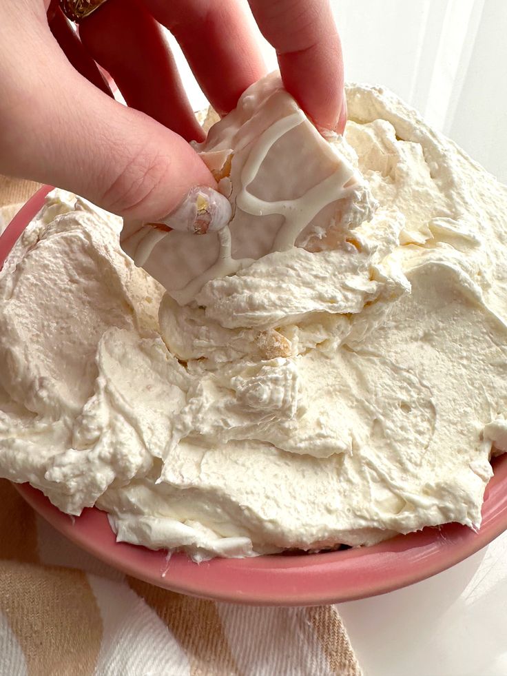 someone is spreading icing on top of a cake in a pink plate with white frosting