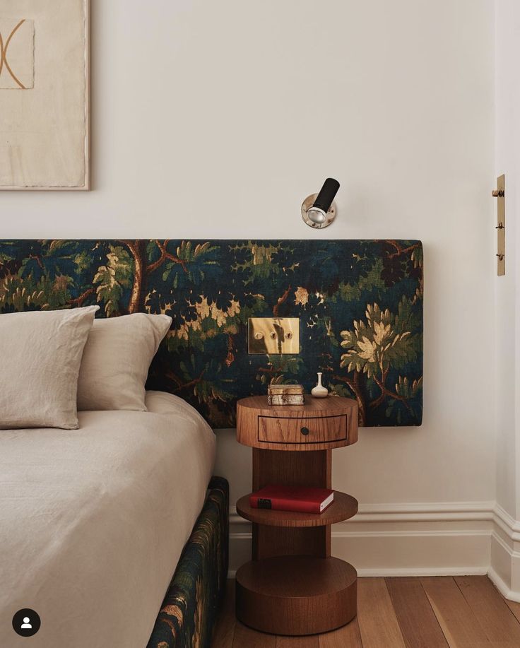 a bed sitting next to a wooden table with a lamp on it's headboard