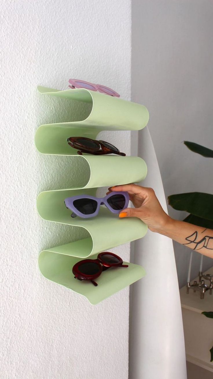 a person is holding up some sunglasses on a rack in front of a white wall