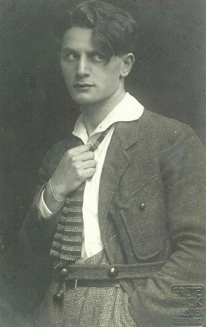 an old black and white photo of a young man tying his tie with one hand