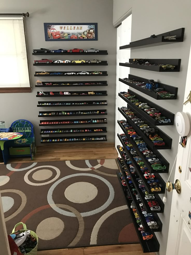 a room filled with lots of toy cars on shelves next to a rug and door