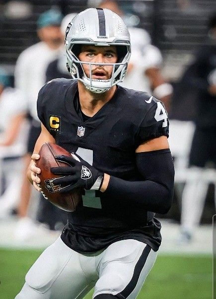 a man holding a football on top of a field with other people in the background