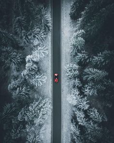 an aerial view of a car driving down a road in the middle of some trees