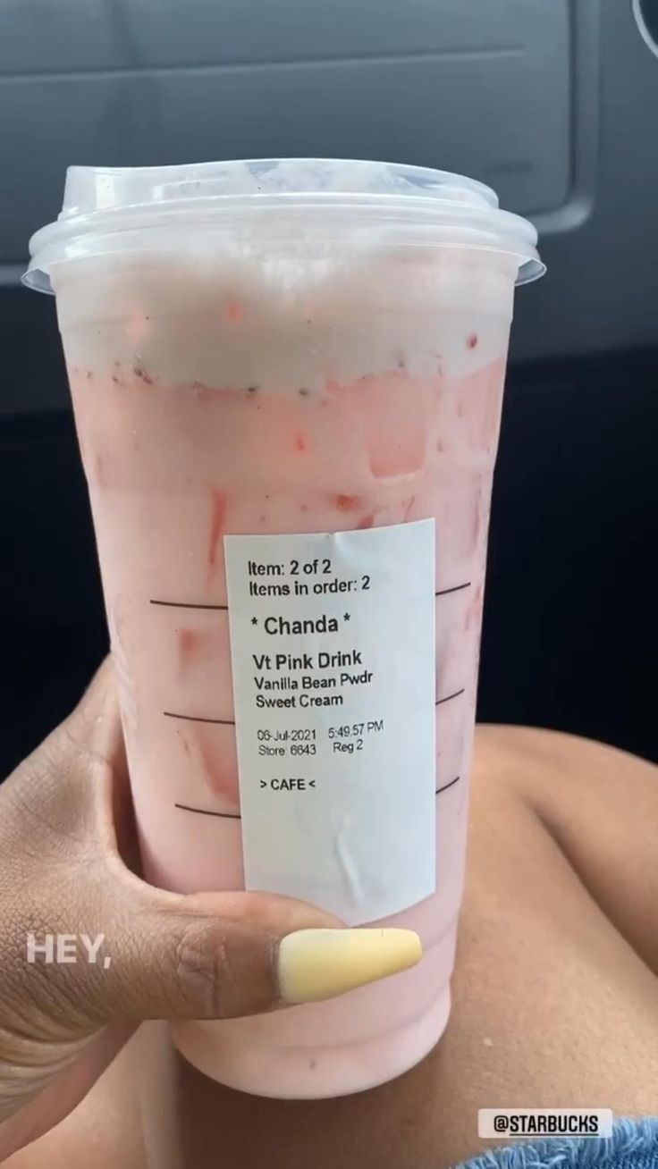 a person holding up a pink drink in the back seat of a car with a label on it