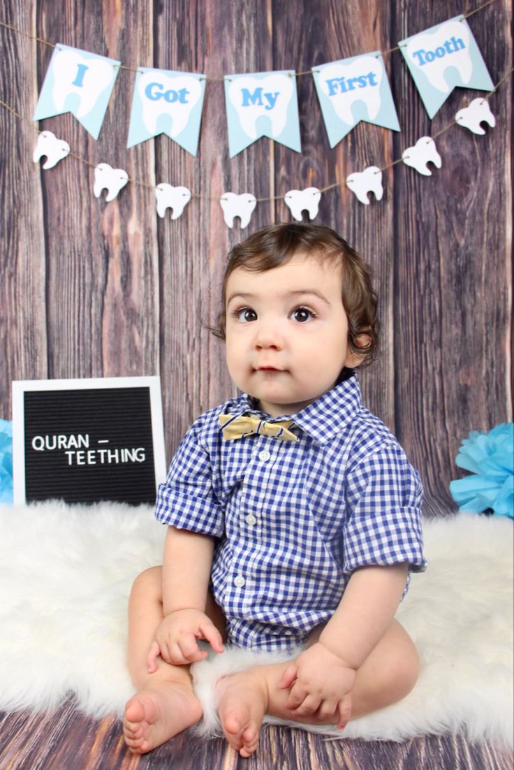 a baby is sitting on the floor in front of a backdrop that says i got my first tooth