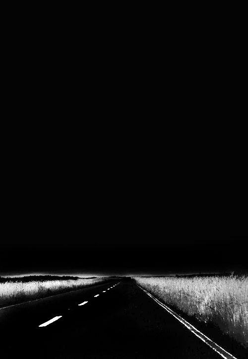 a black and white photo of an empty road at night with the headlights turned on