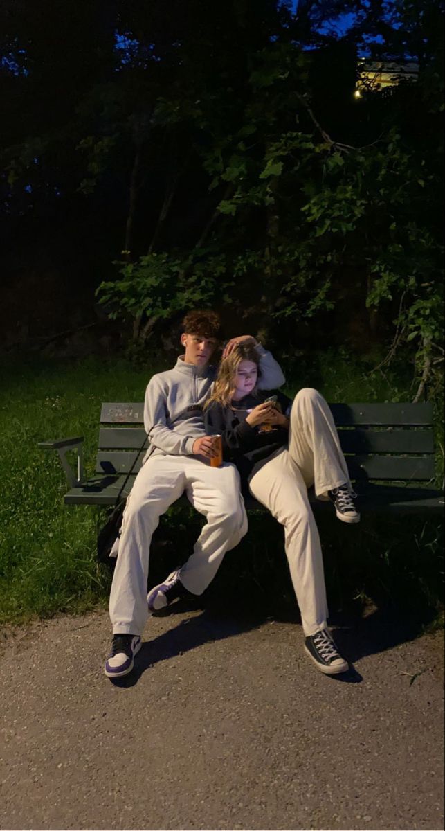 two people are sitting on a bench in the park, one is holding his arm around the other