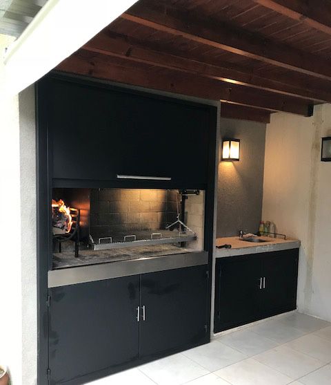 an outdoor kitchen with black cabinets and white tile flooring is seen from the outside