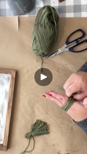 a woman is knitting yarn with scissors on a table next to a wooden frame and some other items