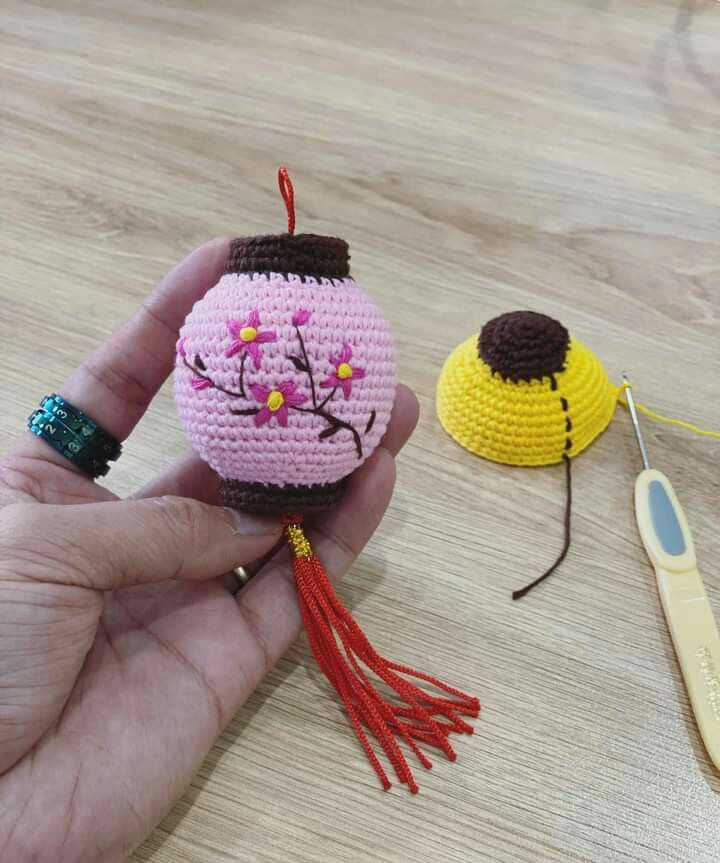 a hand holding a tiny crochet doll next to a needle and thread holder