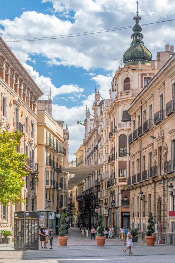 people are walking down the street in an old european city with tall buildings on either side