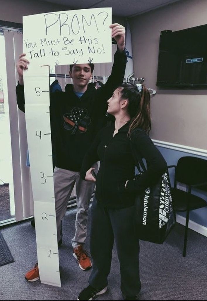 two people standing next to each other holding up a sign with the words prom written on it