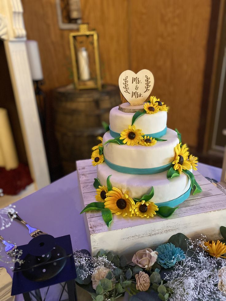 a three tiered cake with sunflowers on the top is sitting on a table