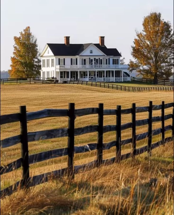 a large white house sitting on top of a lush green field next to a wooden fence