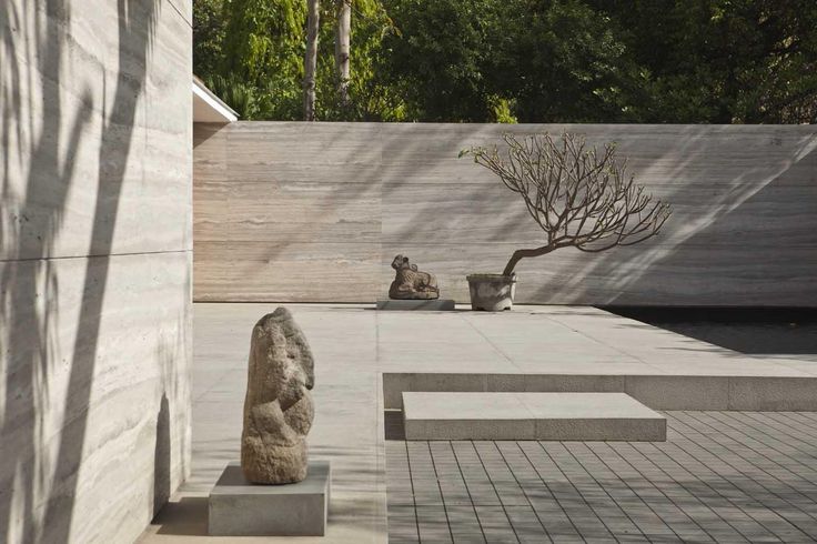 two stone sculptures sitting on cement blocks in front of a wall with trees behind them