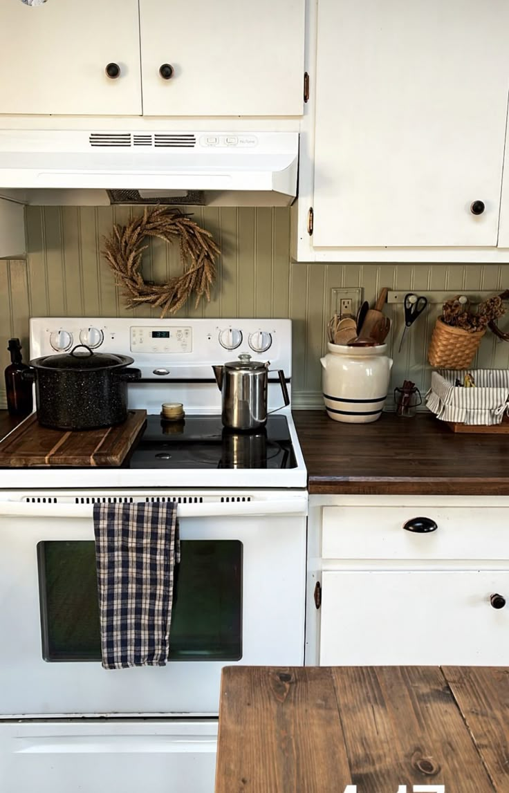 a white stove top oven sitting in a kitchen next to a wooden table and cabinets