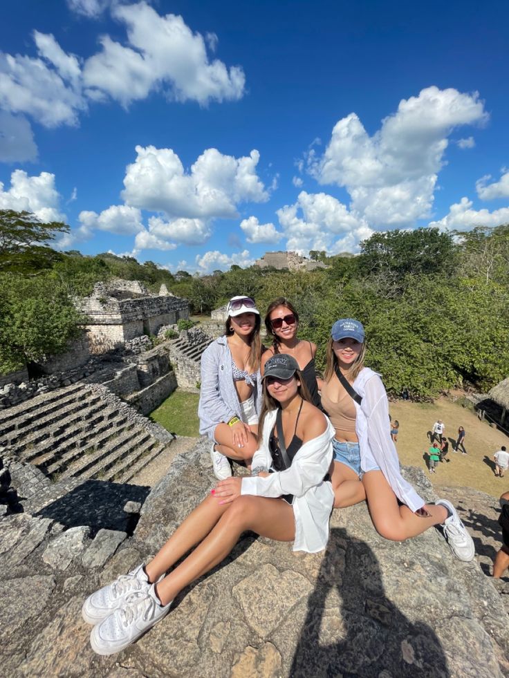 three young women sitting on top of a large rock