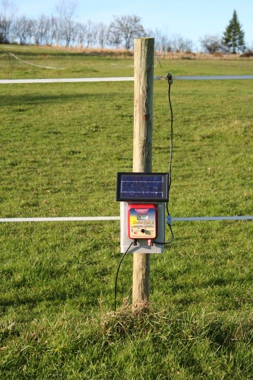 an electronic device attached to a wooden post in a grassy field with wires running through it