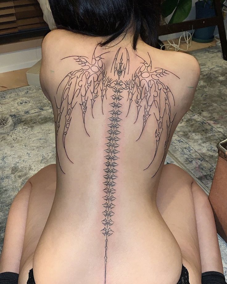 a woman sitting on the floor with her back turned to show an intricate tattoo design