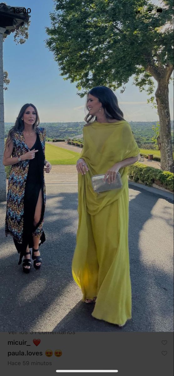 two women are walking down the street in dresses and one is wearing a yellow shawl