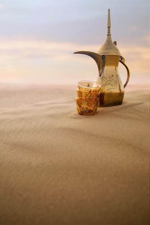 an old fashioned tea pot and two cups in the middle of desert sand with sky background