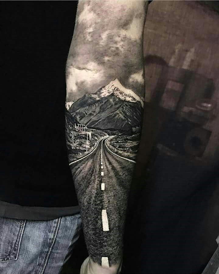 a man's arm with a mountain and road tattoo on it