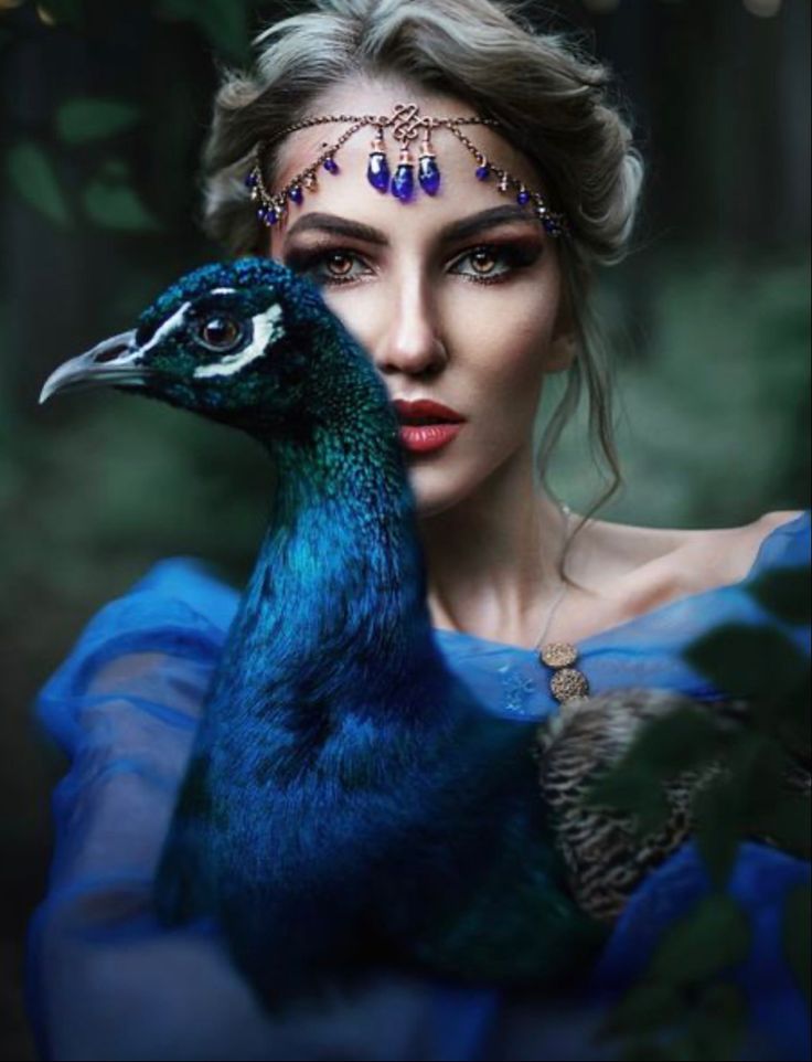 a woman in blue dress holding a peacock with feathers on it's head and eyes