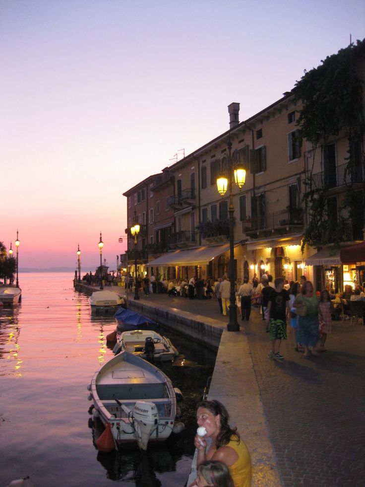 people are standing on the dock near boats and buildings at dusk, with one person taking a photo