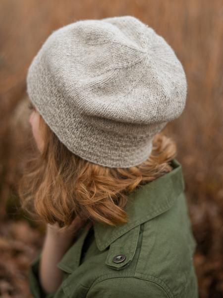 a woman with red hair wearing a gray knitted hat and green jacket in front of brown grass