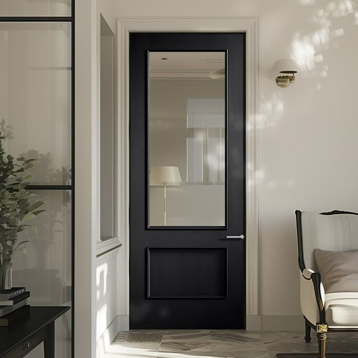 a black door in a white room next to a chair and table with a lamp on it