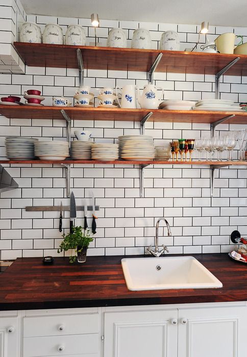 a kitchen with white brick walls and wooden shelves filled with dishes, cups, and utensils