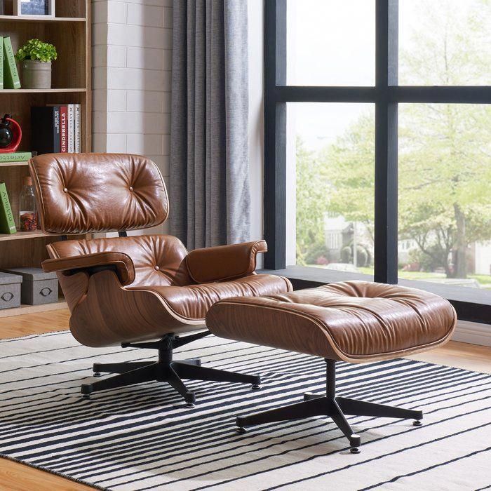 an eames chair and ottoman in front of a large window with bookshelves