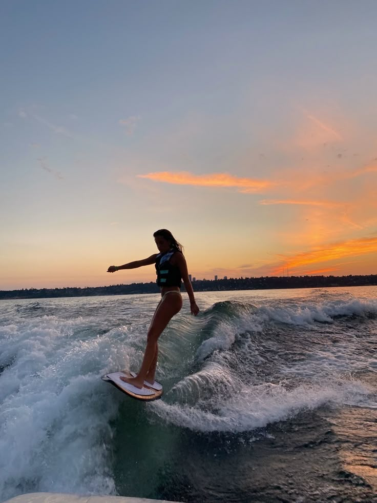 a woman riding a surfboard on top of a wave in the ocean at sunset