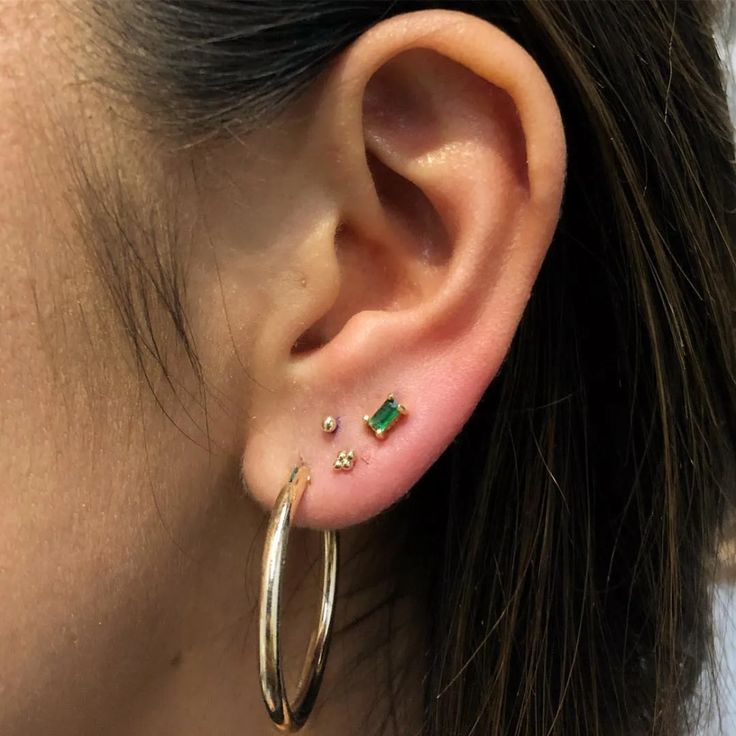 a woman wearing gold hoop earrings with green stones on the inside of her ears and behind her ear