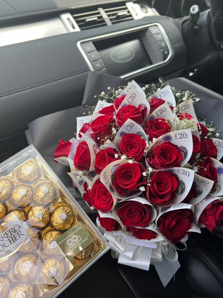 a bouquet of red roses sitting next to a box of chocolates in a car