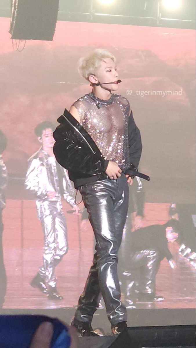 a male in a black shirt and silver pants on a stage with a crowd behind him