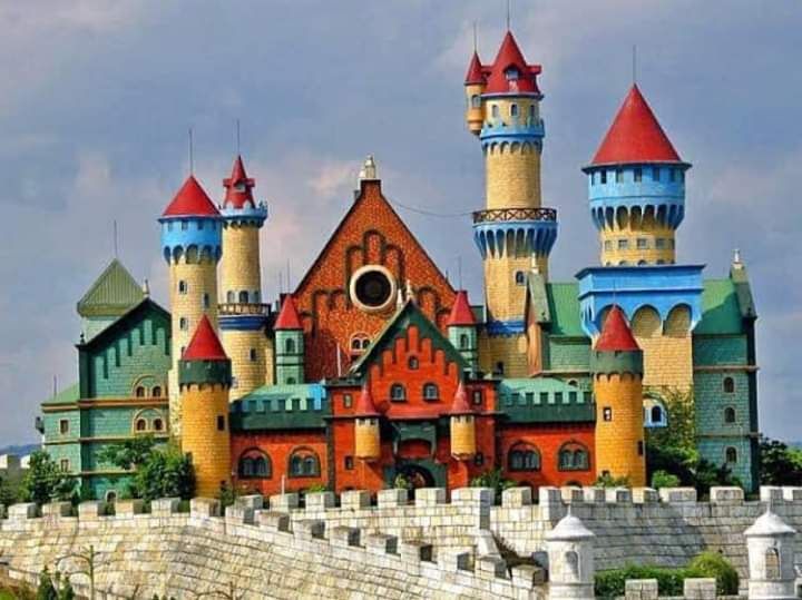 a castle with many towers and windows on top of a rock wall in front of a cloudy sky