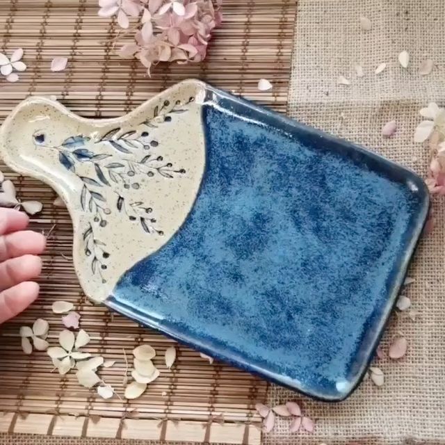 a hand is holding a blue and white dish on a mat with flowers scattered around it