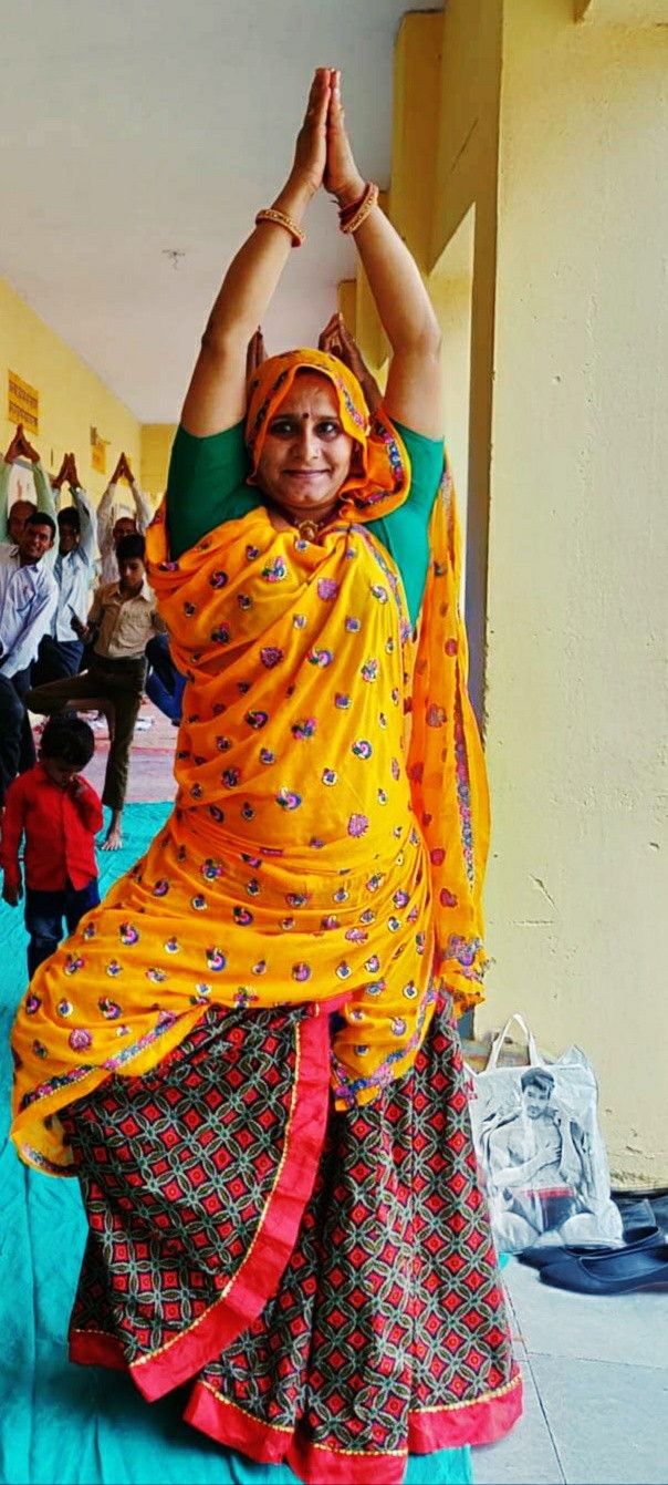 a woman in an orange and green dress is doing yoga poses with her hands up