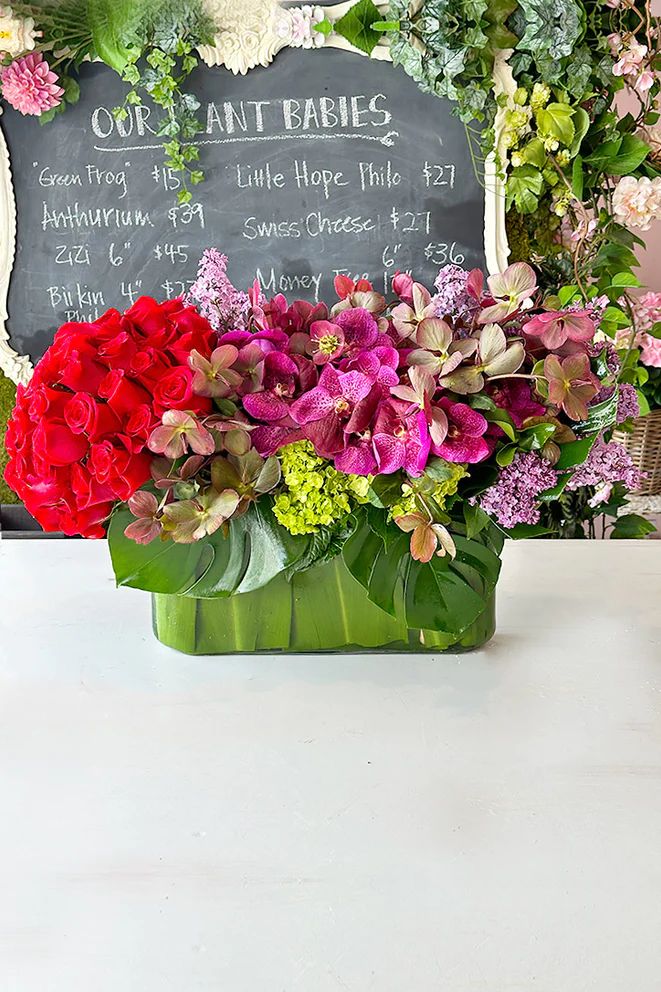 a vase filled with lots of flowers sitting on top of a table next to a chalkboard