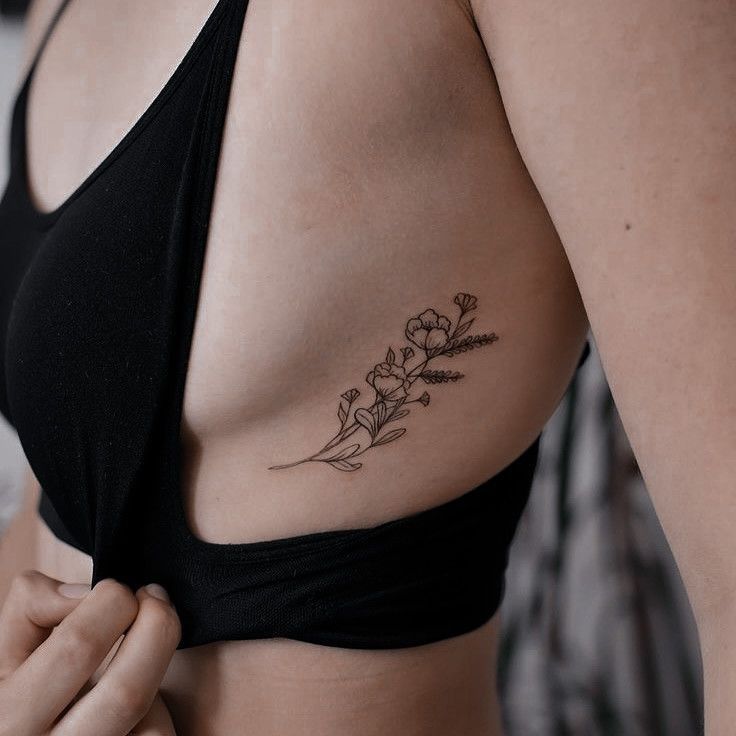 a woman with a flower tattoo on her left side ribcage, showing the breast area