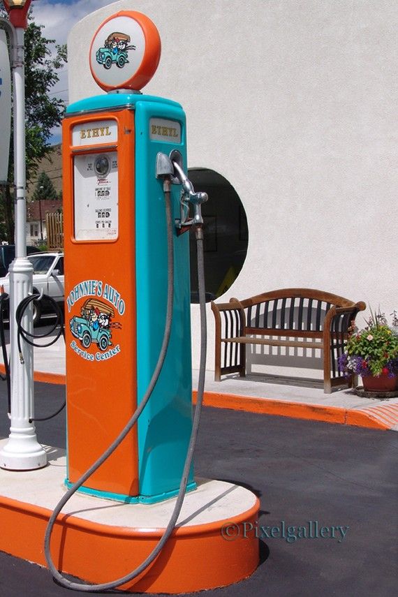 an orange and blue gas pump sitting on top of a cement slab next to a bench