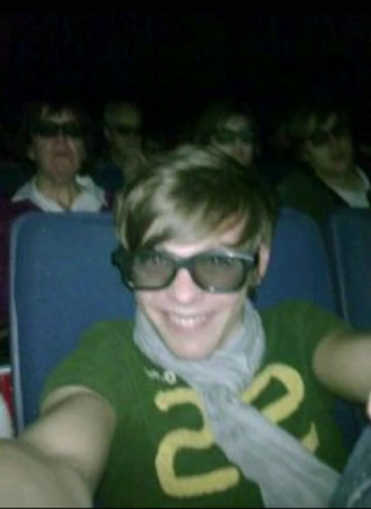 a man wearing sunglasses and scarf sitting in front of an audience at a movie theater