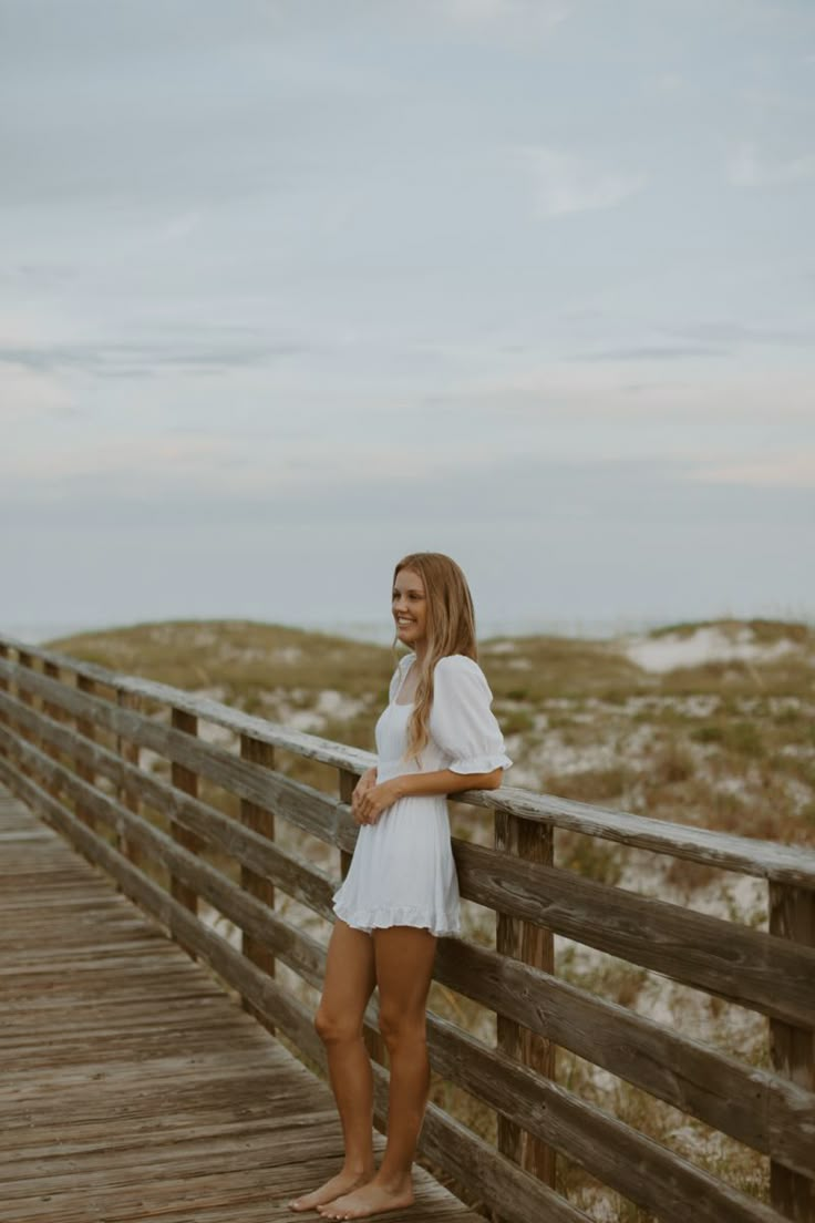 a woman standing on a boardwalk near the beach