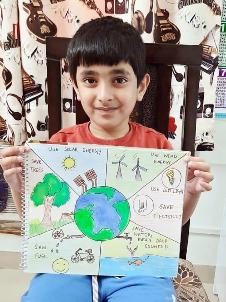 a young boy sitting in a chair holding up a paper with an image of the earth on it